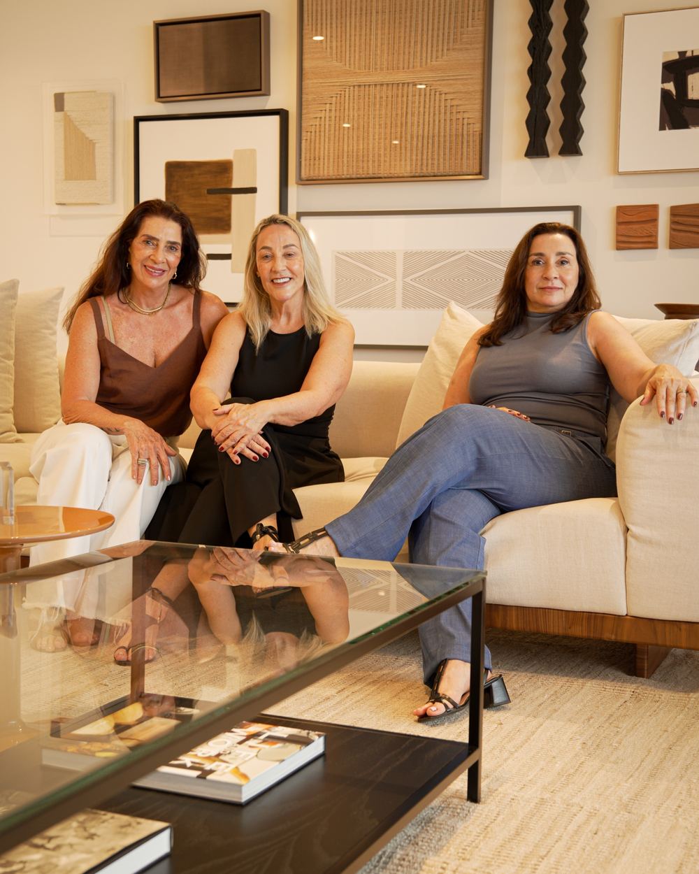 Samira, Mary e Martha, sócias da MJS Rio Imóveis, sentadas em um sofá claro em uma sala decorada em tons de bege e marrom